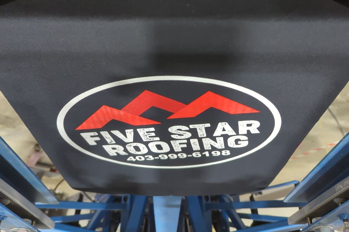 Screen printing press printing a company logo on a black shirt